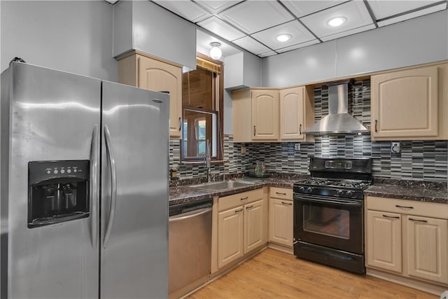 kitchen featuring light brown cabinetry, appliances with stainless steel finishes, wall chimney range hood, and light hardwood / wood-style flooring