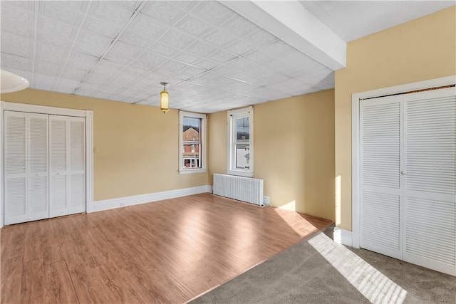 unfurnished bedroom featuring two closets, radiator heating unit, and hardwood / wood-style flooring