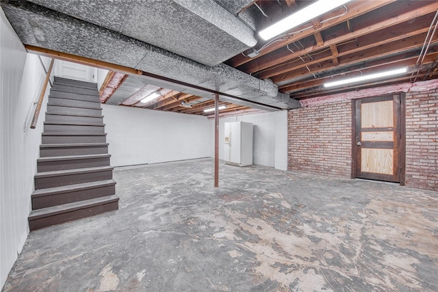 basement with brick wall and white refrigerator with ice dispenser