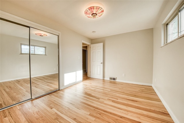 unfurnished bedroom with light hardwood / wood-style floors, multiple windows, and a closet