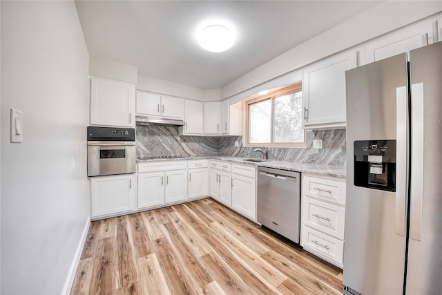 kitchen with white cabinets, stainless steel appliances, backsplash, and light hardwood / wood-style floors