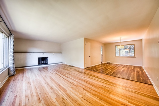 unfurnished living room featuring light hardwood / wood-style flooring and a brick fireplace