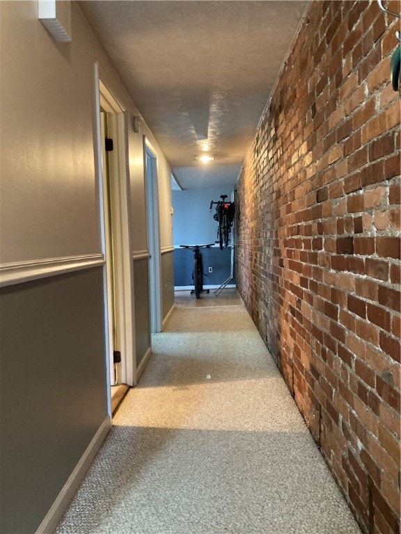 corridor featuring brick wall, a textured ceiling, and light colored carpet