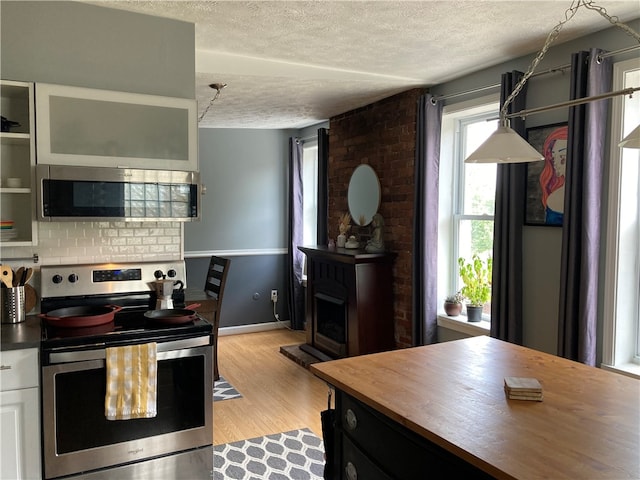 kitchen featuring appliances with stainless steel finishes, light wood-type flooring, a textured ceiling, hanging light fixtures, and white cabinetry