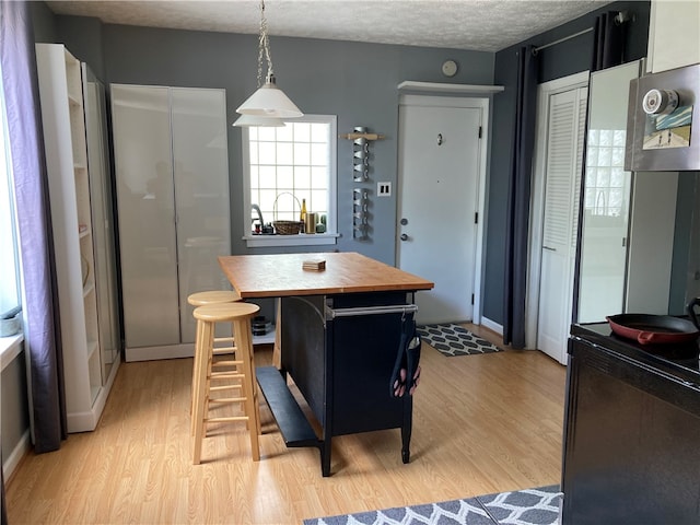 kitchen featuring a textured ceiling, decorative light fixtures, light wood-type flooring, and butcher block countertops