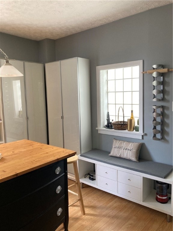 interior space with butcher block counters, pendant lighting, light wood-type flooring, white cabinets, and a textured ceiling