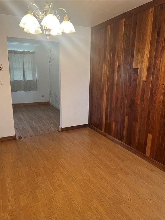 empty room with hardwood / wood-style flooring, wood walls, and a notable chandelier