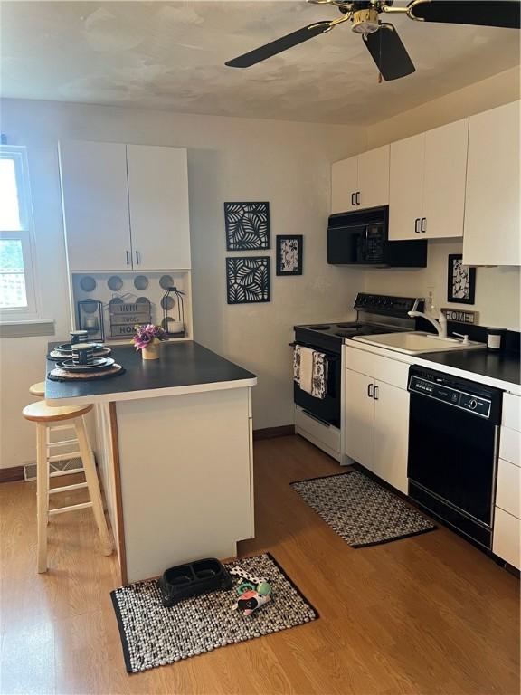 kitchen featuring a breakfast bar area, white cabinetry, black appliances, and wood-type flooring