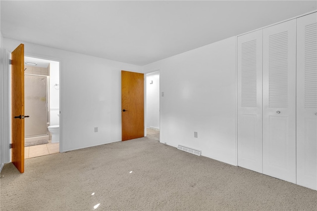 unfurnished bedroom with light carpet, a closet, and ensuite bath