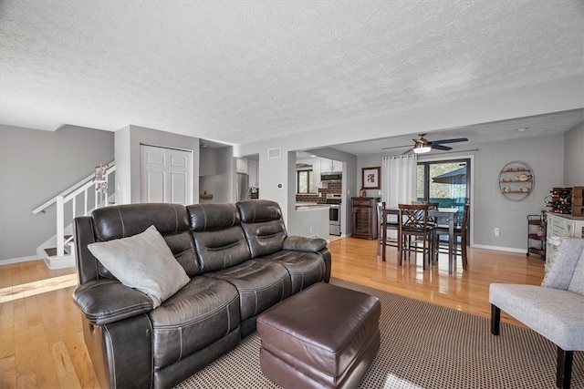 living room featuring light hardwood / wood-style floors, a textured ceiling, and ceiling fan