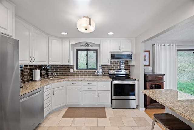 kitchen featuring tasteful backsplash, light stone countertops, appliances with stainless steel finishes, sink, and white cabinetry