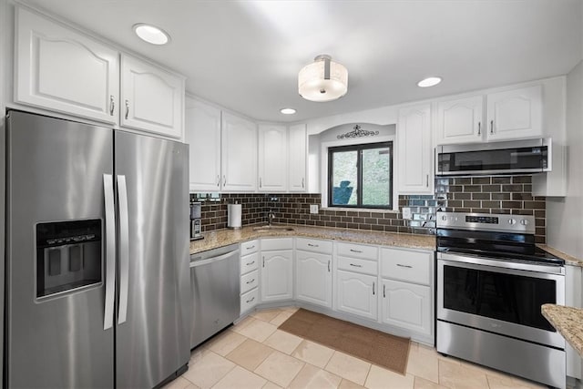 kitchen with tasteful backsplash, light stone countertops, appliances with stainless steel finishes, light tile patterned flooring, and white cabinets