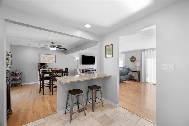 kitchen with a breakfast bar area, a textured ceiling, light wood-type flooring, and ceiling fan