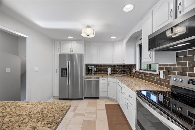 kitchen featuring tasteful backsplash, light stone countertops, stainless steel appliances, white cabinets, and exhaust hood