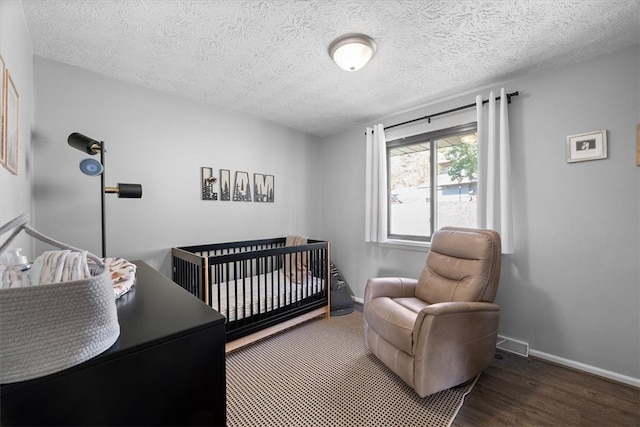 bedroom with a nursery area, a textured ceiling, and dark hardwood / wood-style floors