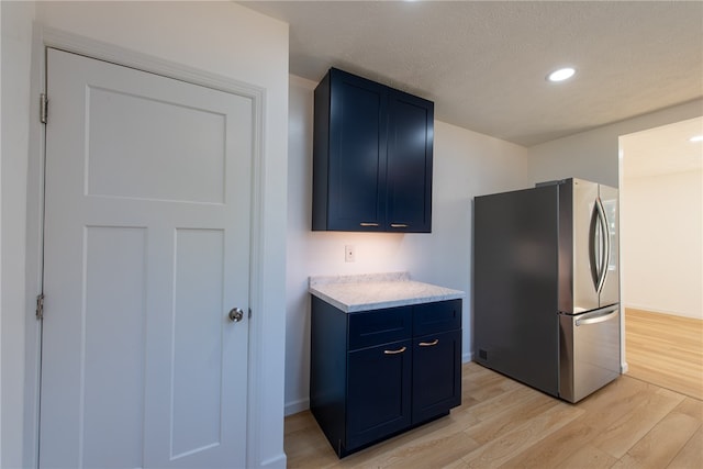 kitchen with blue cabinetry, a textured ceiling, light wood-type flooring, and stainless steel refrigerator