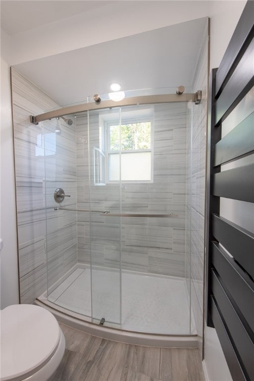 bathroom with a shower with door, hardwood / wood-style floors, and toilet