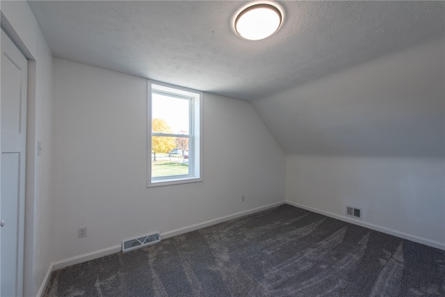 additional living space featuring dark carpet, lofted ceiling, and a textured ceiling