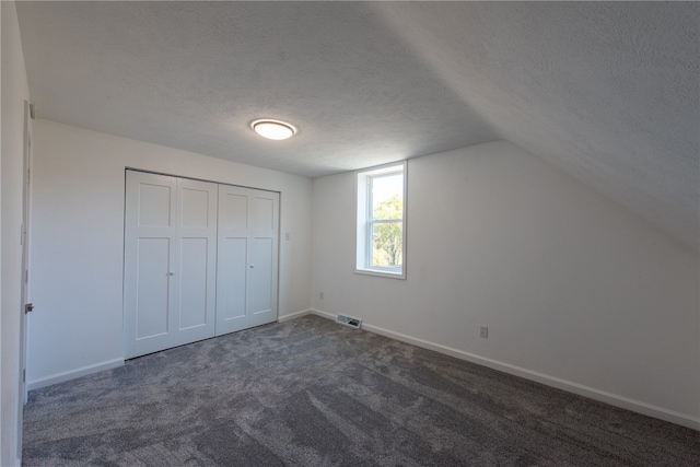 unfurnished bedroom with a closet, a textured ceiling, dark carpet, and vaulted ceiling