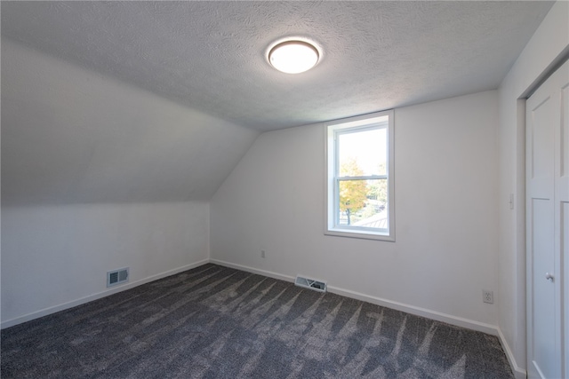 bonus room featuring a textured ceiling, vaulted ceiling, and dark colored carpet