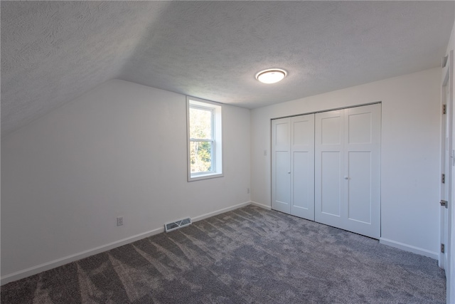 unfurnished bedroom with a closet, a textured ceiling, lofted ceiling, and dark colored carpet