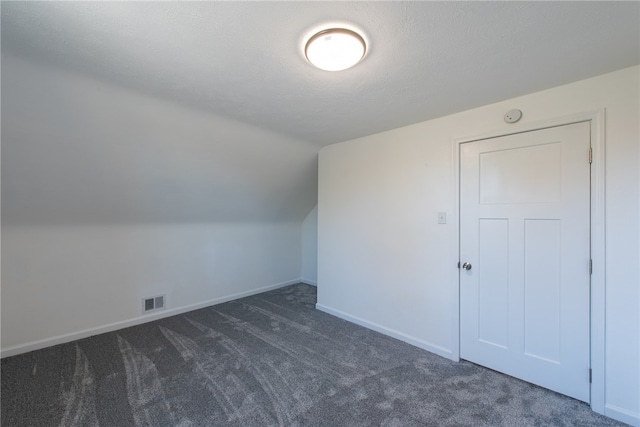 bonus room featuring lofted ceiling, dark colored carpet, and a textured ceiling