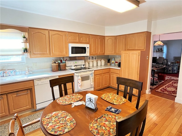 kitchen featuring white appliances, sink, hanging light fixtures, light hardwood / wood-style flooring, and tasteful backsplash