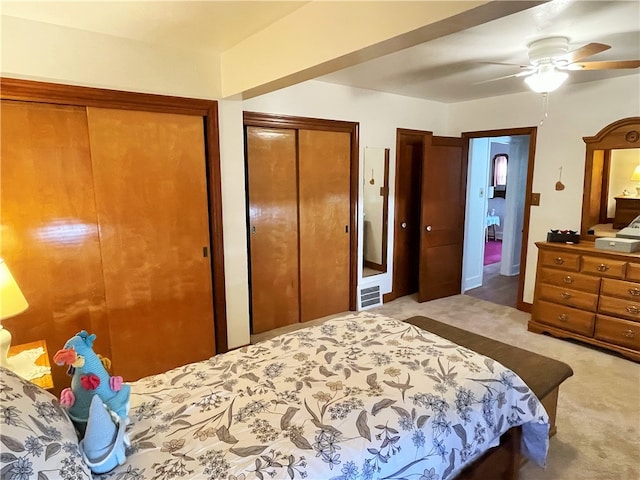 bedroom featuring ceiling fan, light colored carpet, and two closets