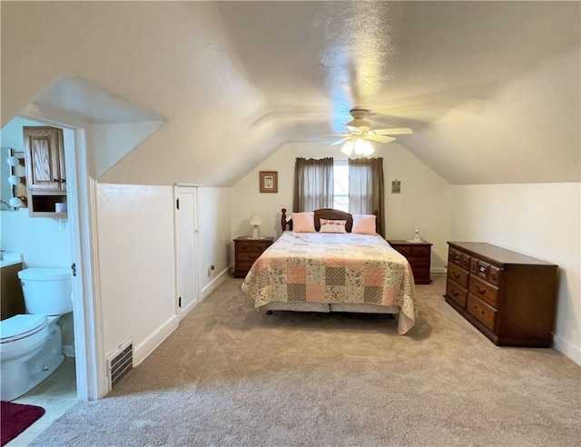 bedroom with ensuite bathroom, ceiling fan, light colored carpet, and vaulted ceiling