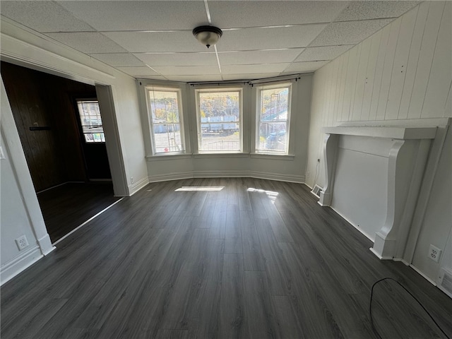 unfurnished dining area with dark wood-type flooring, a drop ceiling, and wooden walls