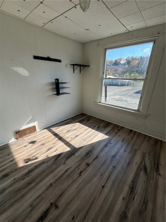 unfurnished room with a drop ceiling, wooden walls, and dark hardwood / wood-style flooring