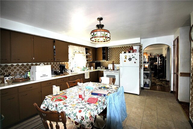 kitchen with white appliances, backsplash, dark brown cabinets, and hanging light fixtures