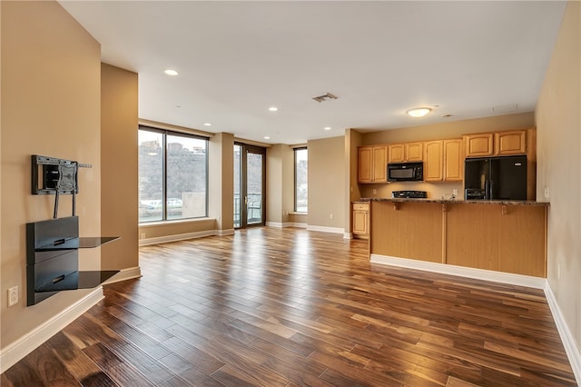 kitchen with light brown cabinetry, black appliances, kitchen peninsula, dark stone countertops, and dark hardwood / wood-style floors