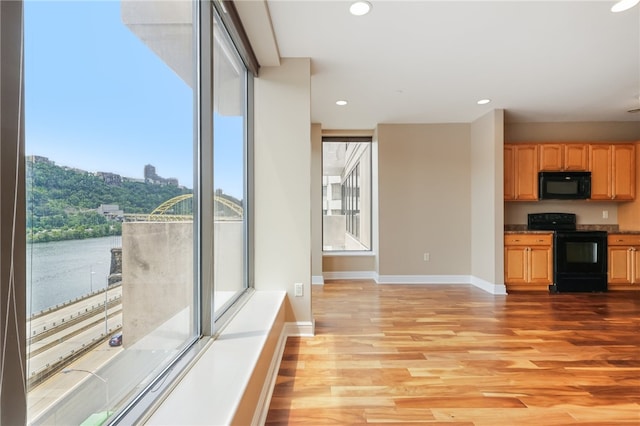 kitchen with a water view, black appliances, and light wood-type flooring