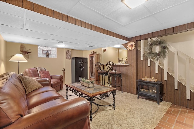 living room featuring a paneled ceiling, a wood stove, and wood walls