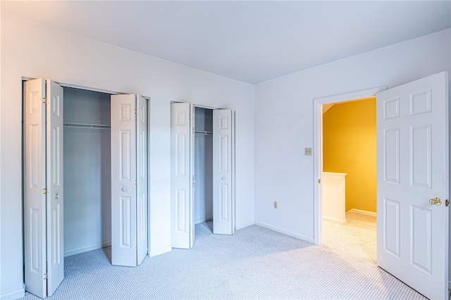 unfurnished bedroom featuring multiple closets and light colored carpet