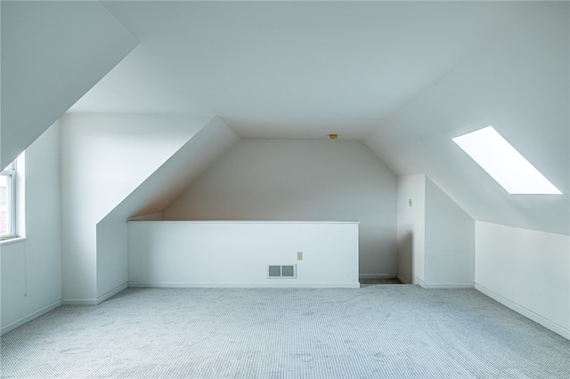 additional living space featuring vaulted ceiling with skylight and light colored carpet