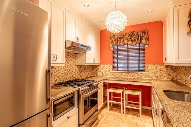 kitchen featuring appliances with stainless steel finishes, sink, light stone counters, decorative backsplash, and an inviting chandelier