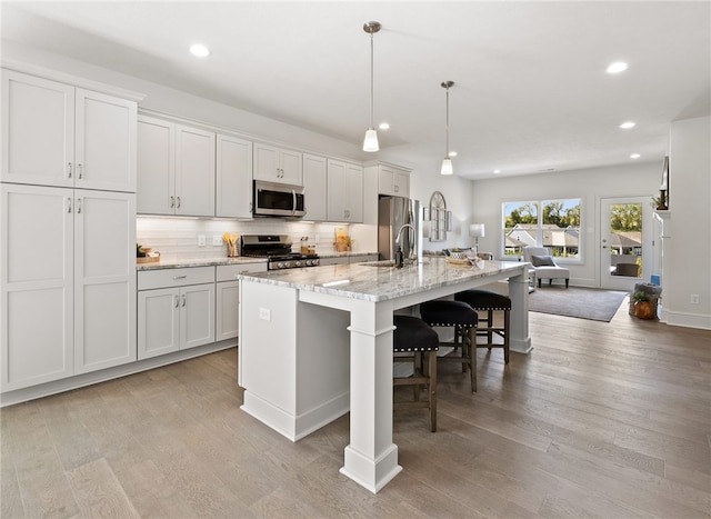 kitchen featuring a breakfast bar area, appliances with stainless steel finishes, a kitchen island with sink, light wood-type flooring, and pendant lighting