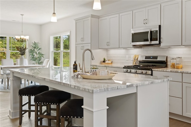 kitchen with tasteful backsplash, light hardwood / wood-style floors, stainless steel appliances, pendant lighting, and a kitchen island with sink