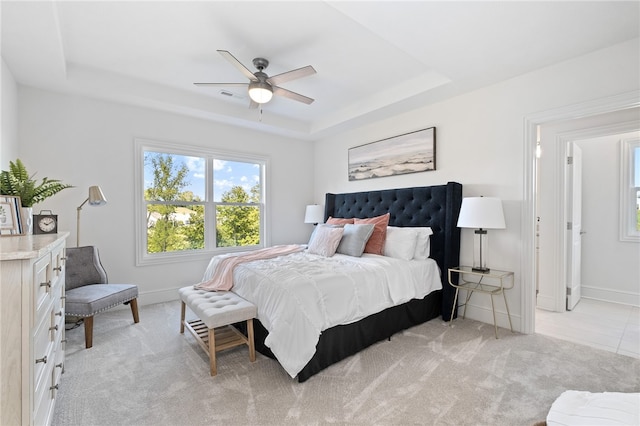 carpeted bedroom with a raised ceiling and ceiling fan