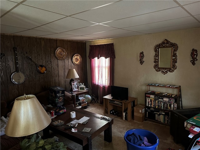 carpeted living room featuring a paneled ceiling and wood walls