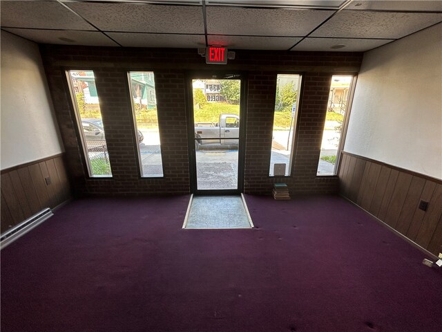 carpeted spare room featuring brick wall, a drop ceiling, and wooden walls