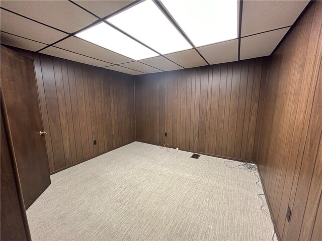 basement featuring light carpet, wood walls, and a paneled ceiling