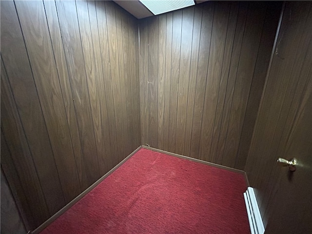 unfurnished room with baseboard heating, wooden walls, and carpet flooring