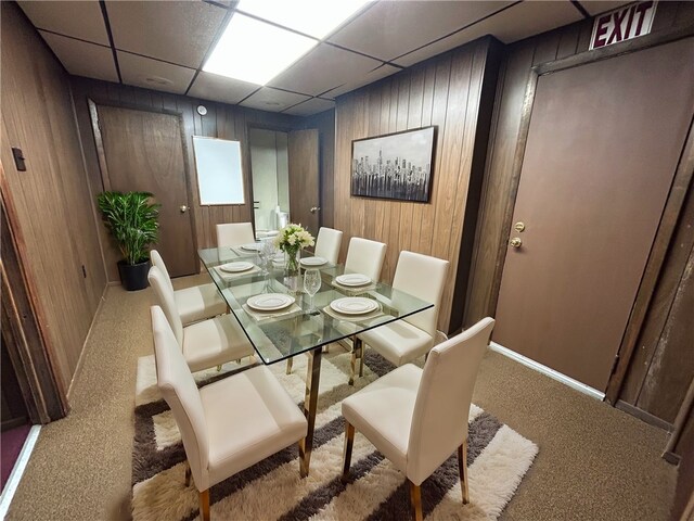 dining space featuring wood walls, carpet flooring, and a paneled ceiling