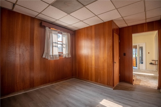 spare room featuring light hardwood / wood-style flooring, a paneled ceiling, and wooden walls