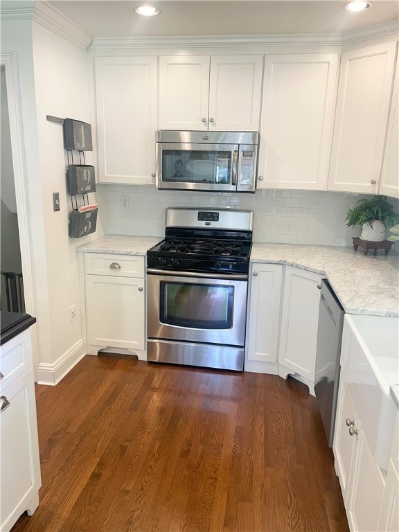 kitchen with dark wood-type flooring, appliances with stainless steel finishes, white cabinetry, and decorative backsplash