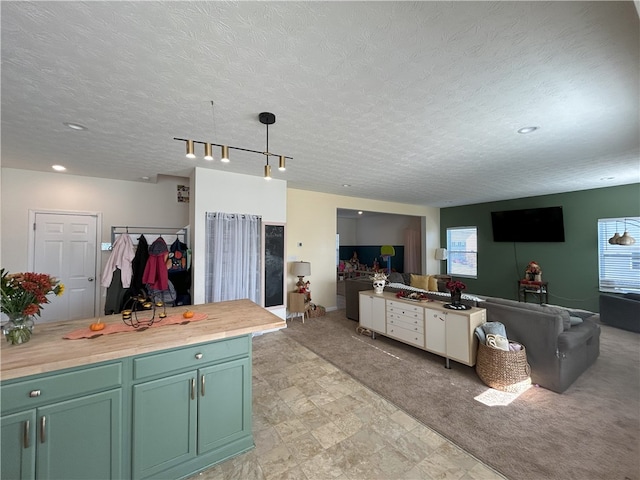 kitchen with hanging light fixtures, green cabinets, butcher block countertops, a textured ceiling, and light carpet