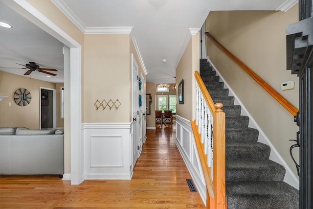 stairs with crown molding, hardwood / wood-style flooring, and ceiling fan with notable chandelier